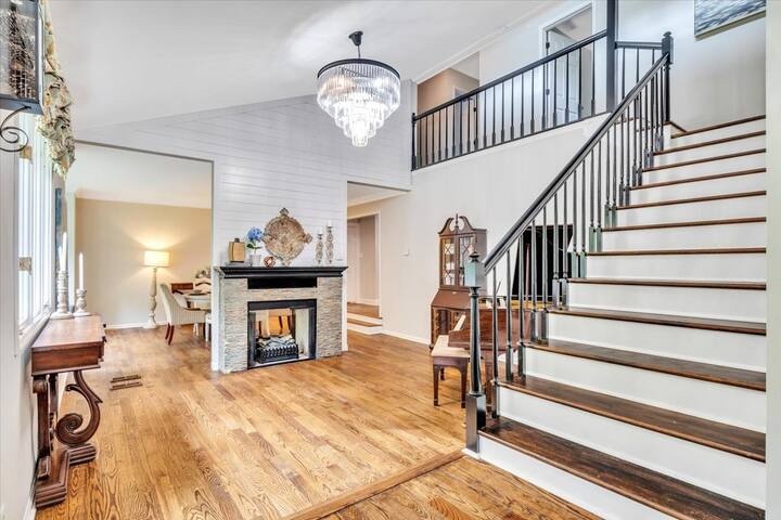 Bright entry hall with wood floors, fireplace, chandelier, and staircase